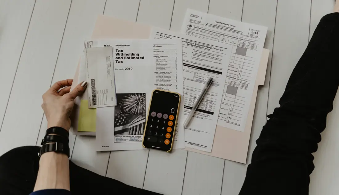 A desk with tax forms, a calculator and a phone, with a person sorting papers